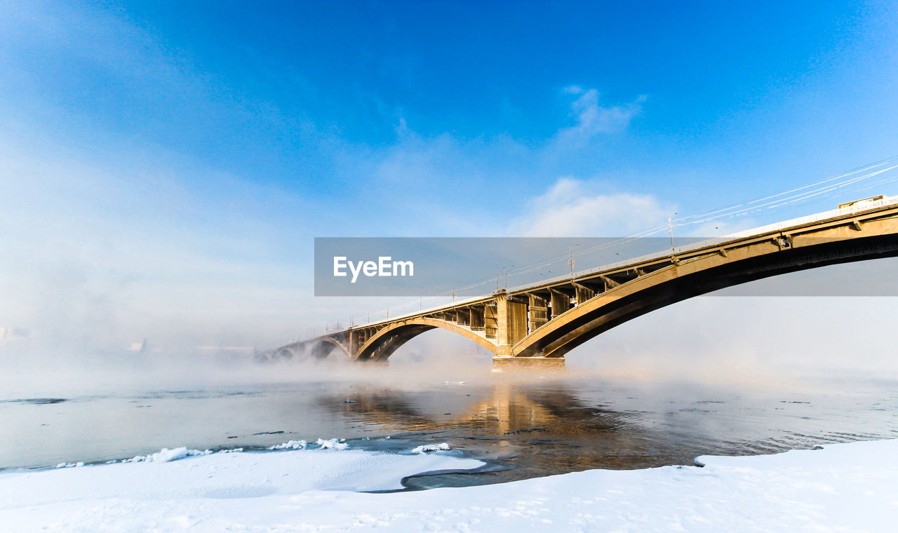 Low angle view of bridge over yenisei river against blue sky on sunny day