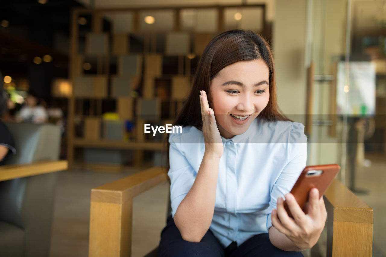 Smiling businesswoman using smart phone while sitting on chair in cafe