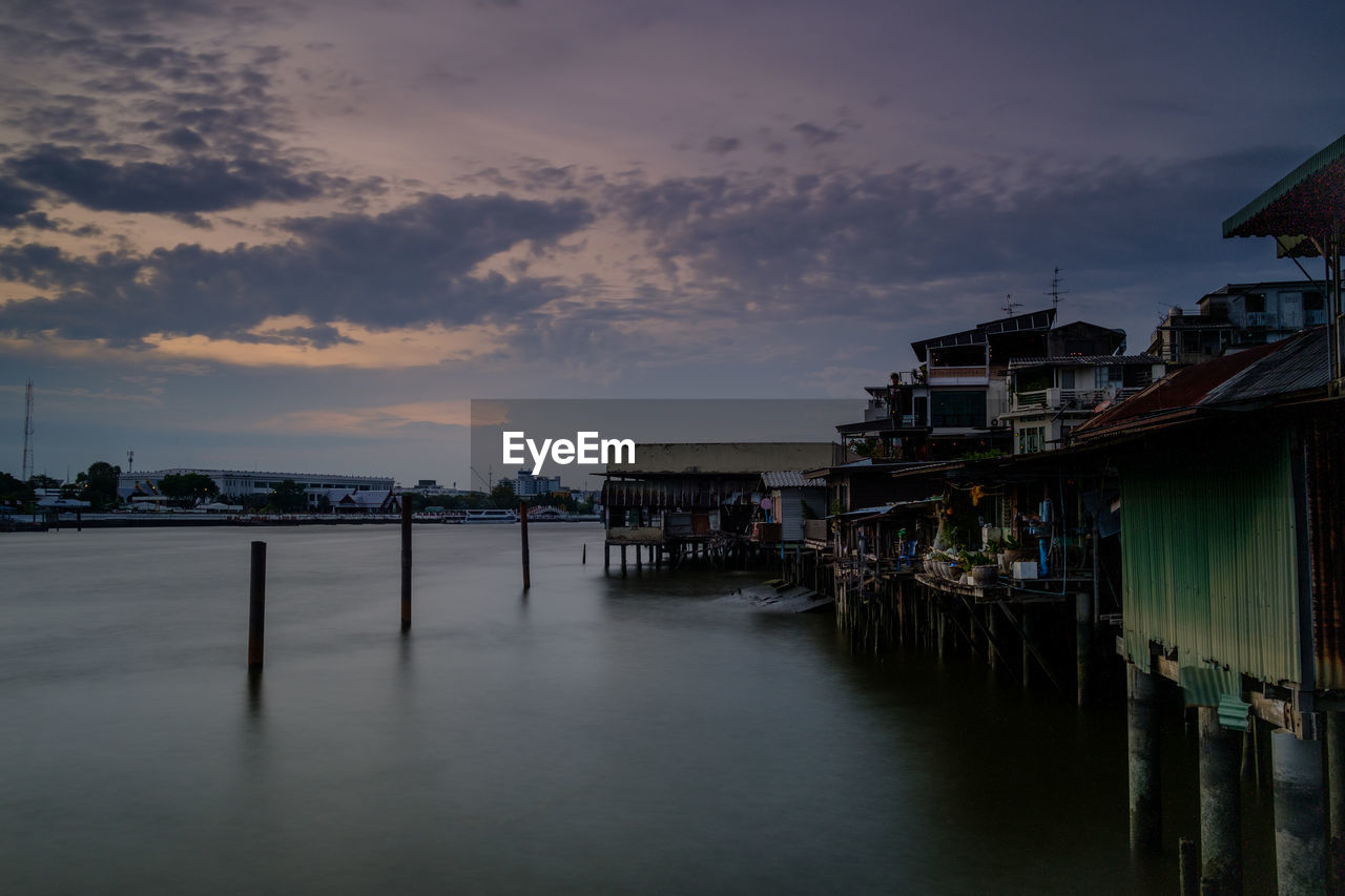 Scenic view of river by buildings against sky during sunset