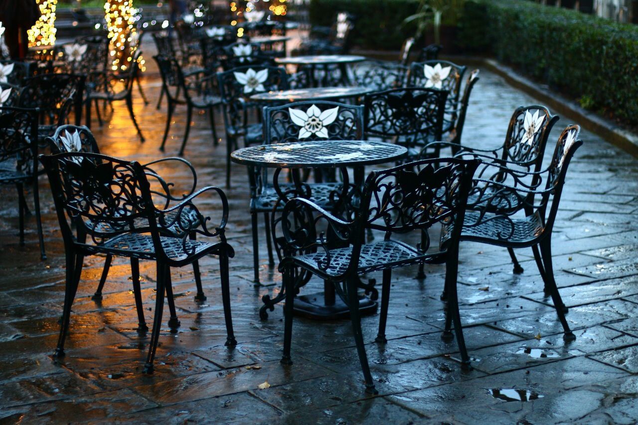 Empty chairs and tables on wet footpath at sidewalk cafe