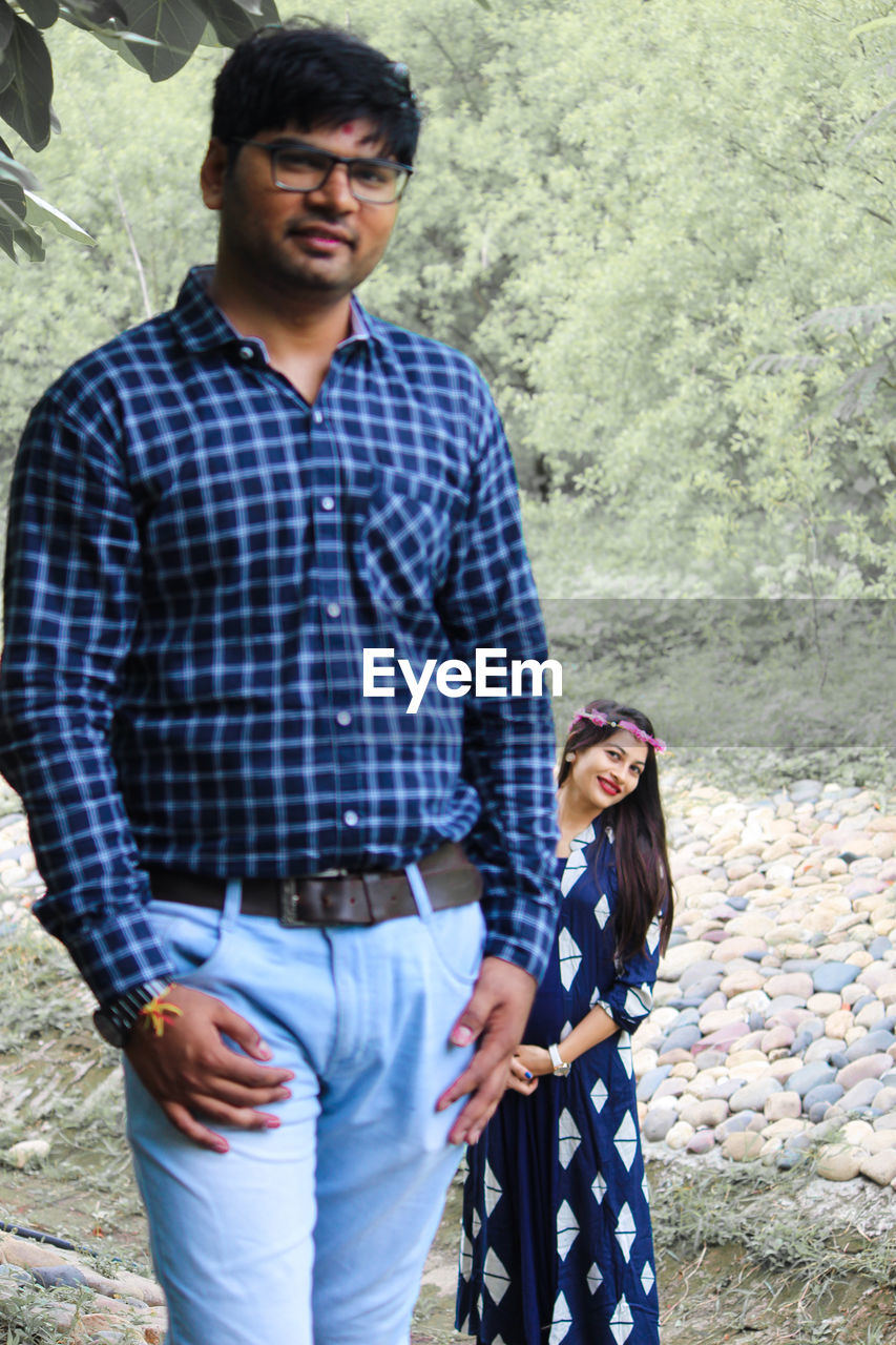 Portrait of young couple standing on land against trees