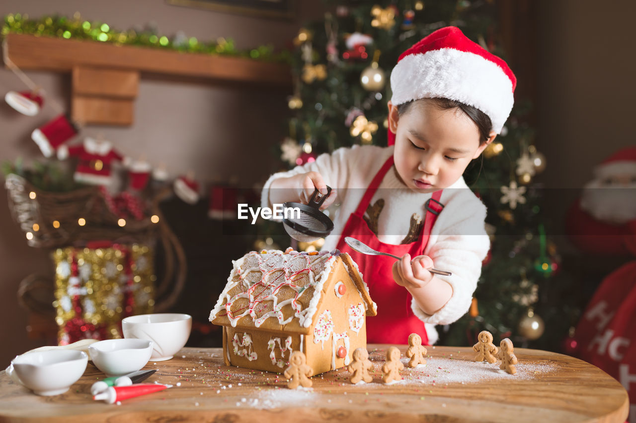 Cute girl preparing gingerbread house at home