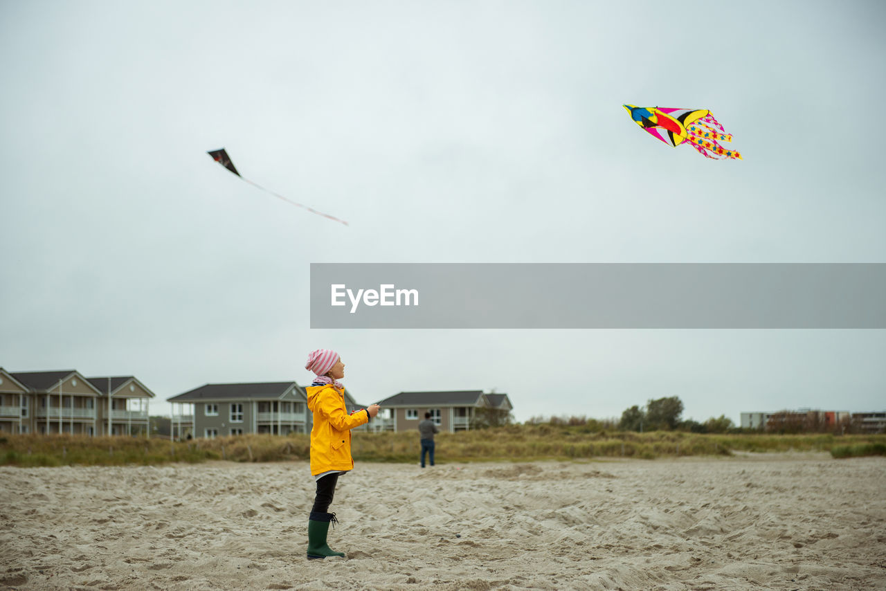 Rear view of boy holding kite standing on beach against sky