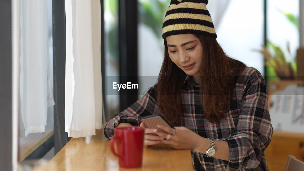 Young woman using mobile phone while sitting on table