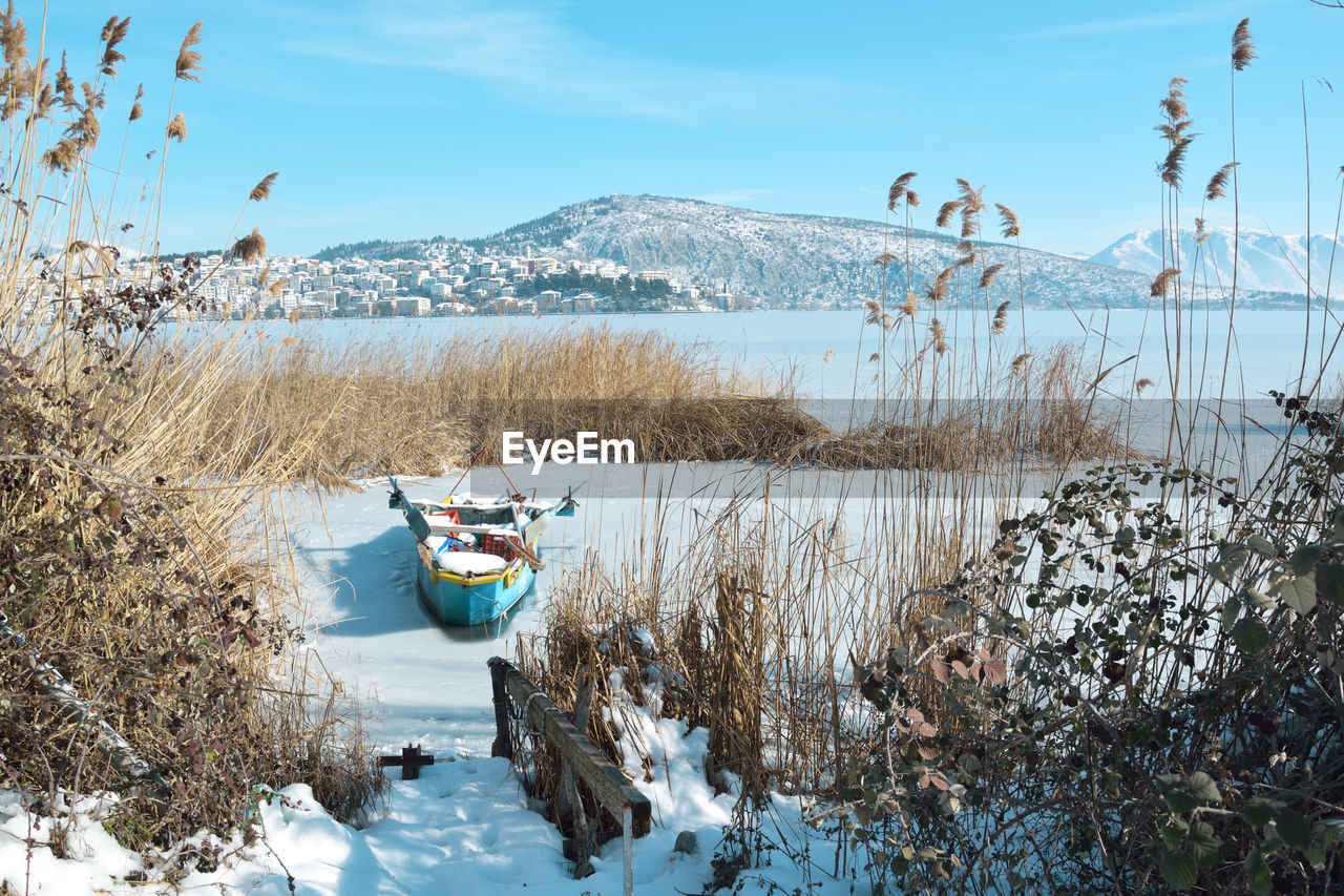 Snowy lake scene with boat trapped in the lake and town of kastoria as background