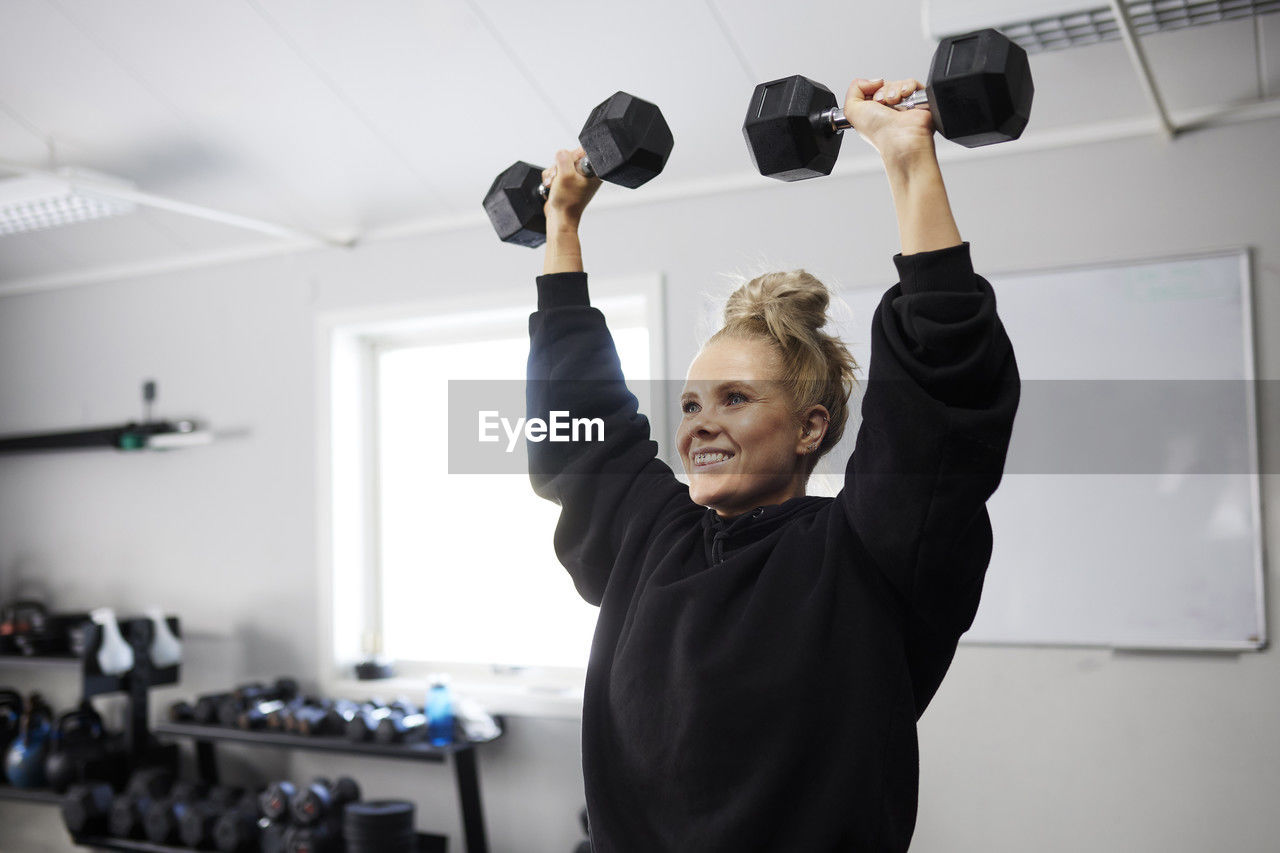 Smiling woman exercising with dumbbells at health club