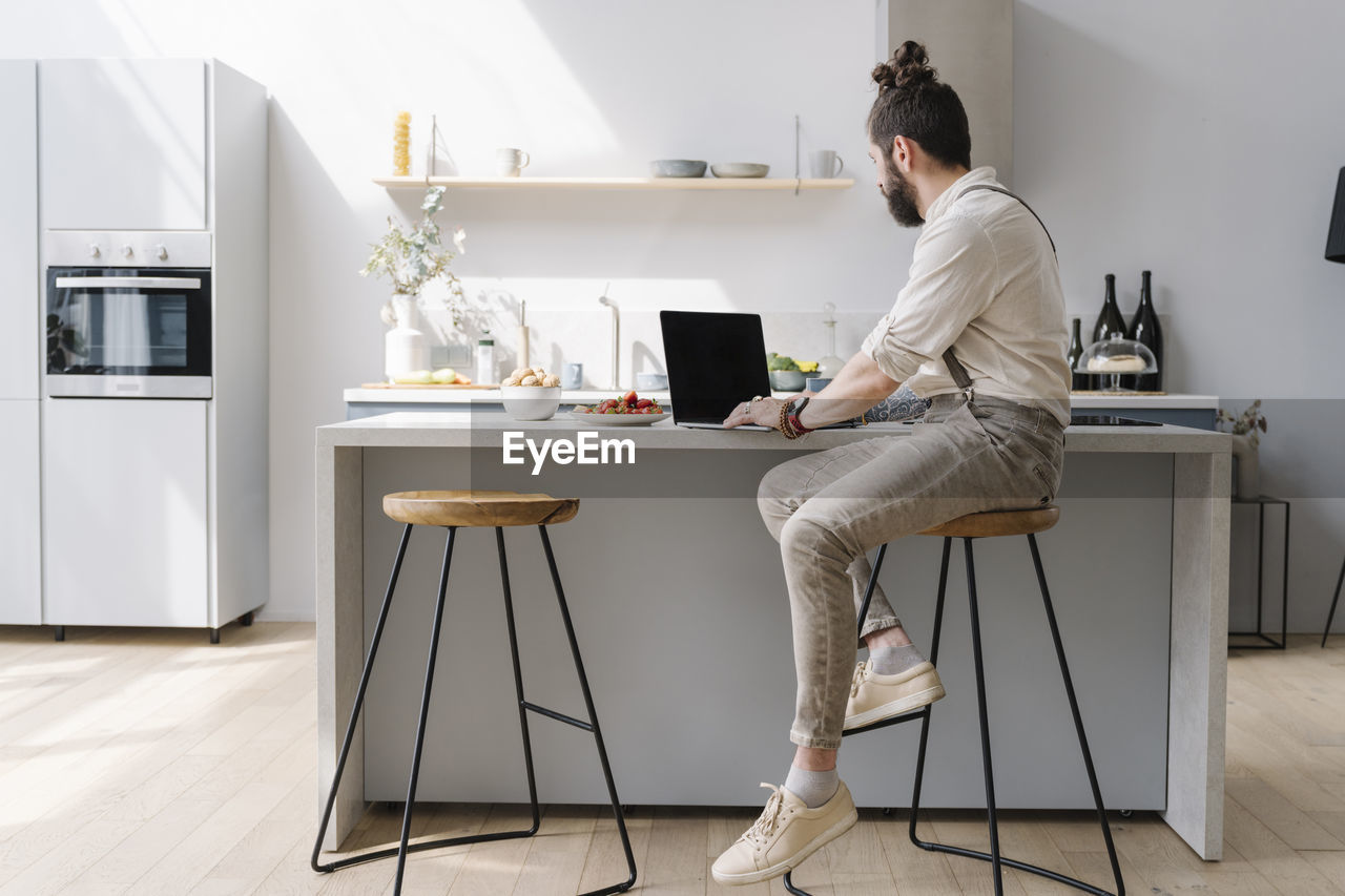 Mid adult man using laptop while sitting in kitchen at home