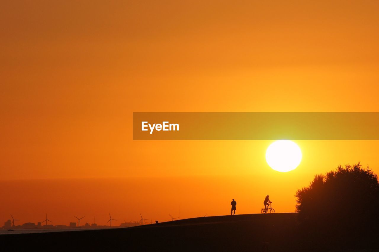 SILHOUETTE MAN ON TREE AGAINST ORANGE SKY