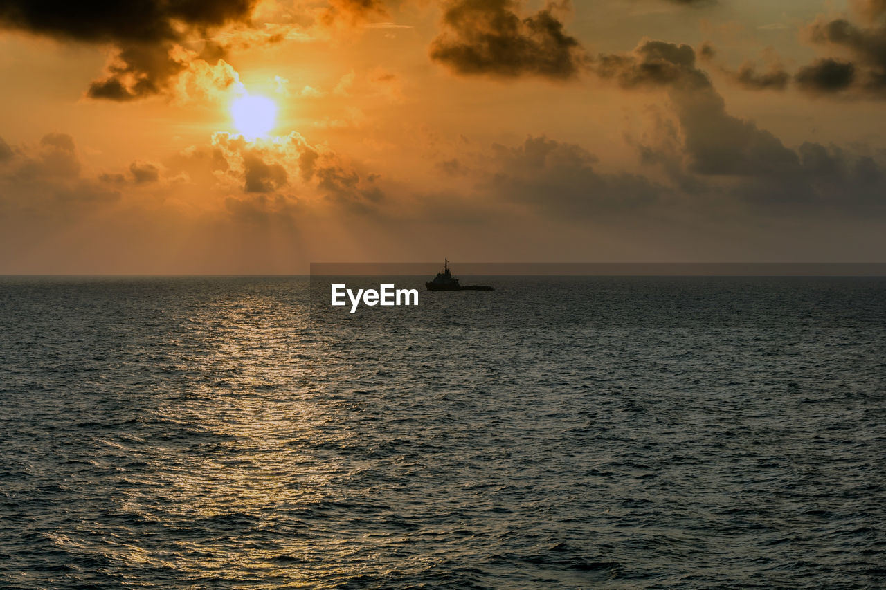 A silhouette of an anchor handling tugboat maneuvering during sunset at offshore oil field