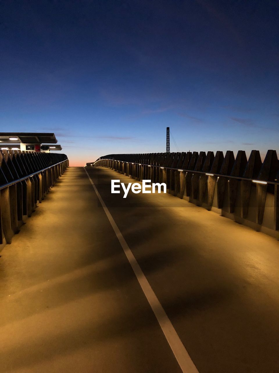 Empty road along bridge at sunset