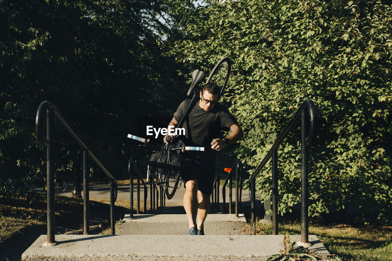 Active male athlete climbing steps while carrying bicycle in park