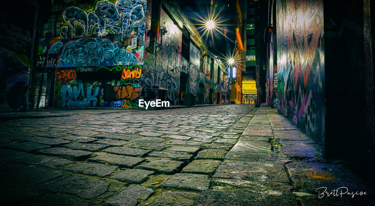 ILLUMINATED STREET AMIDST BUILDINGS AT NIGHT