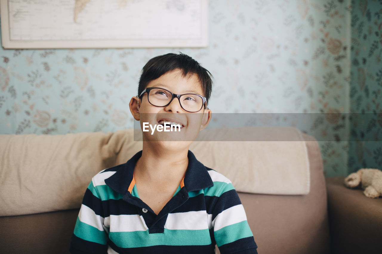 Thoughtful disabled boy laughing while sitting on sofa at home