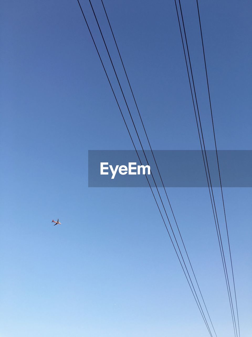 Low angle view of airplane and cables against clear blue sky