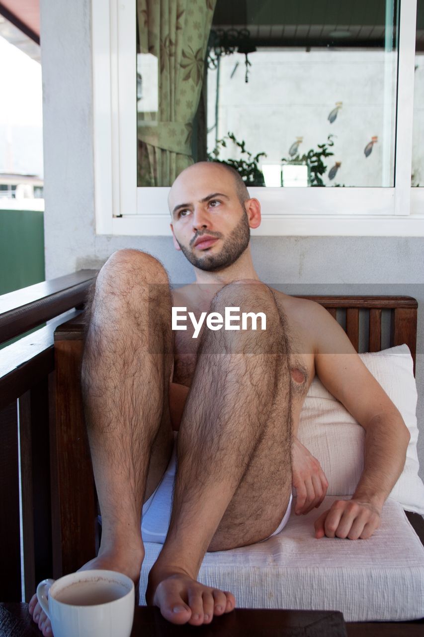 Shirtless man looking away while sitting at home