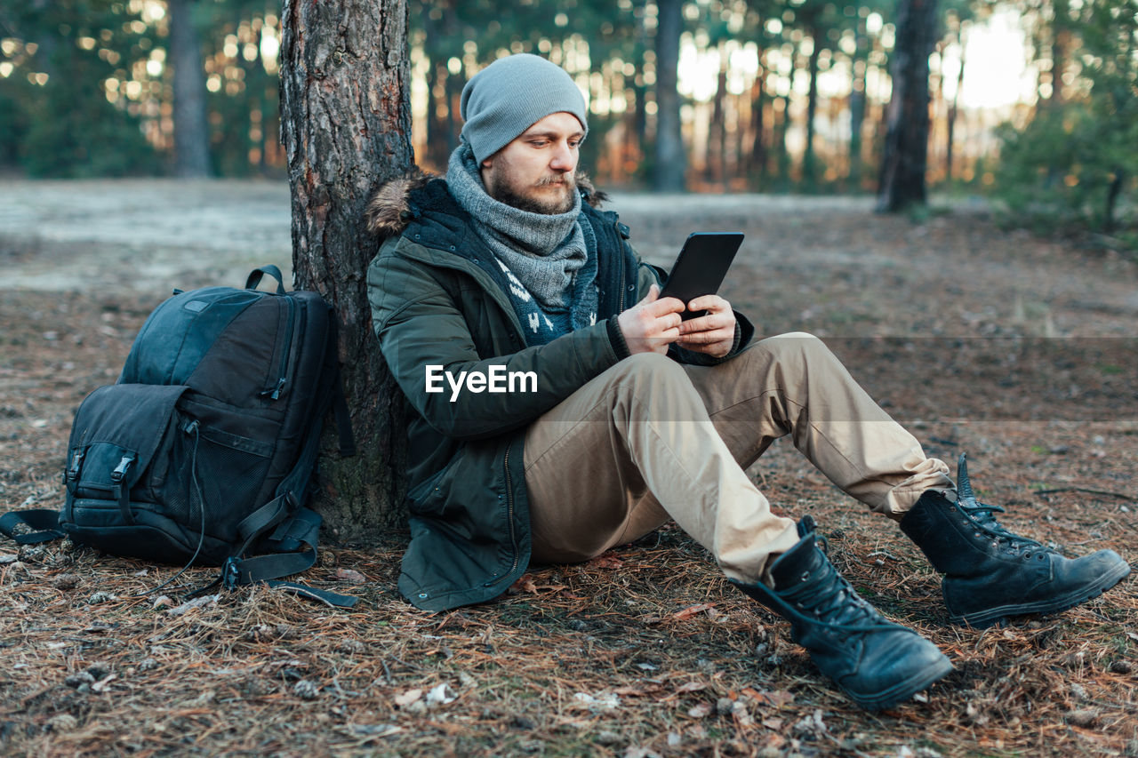 Full length of male hiker using digital tablet while sitting in forest