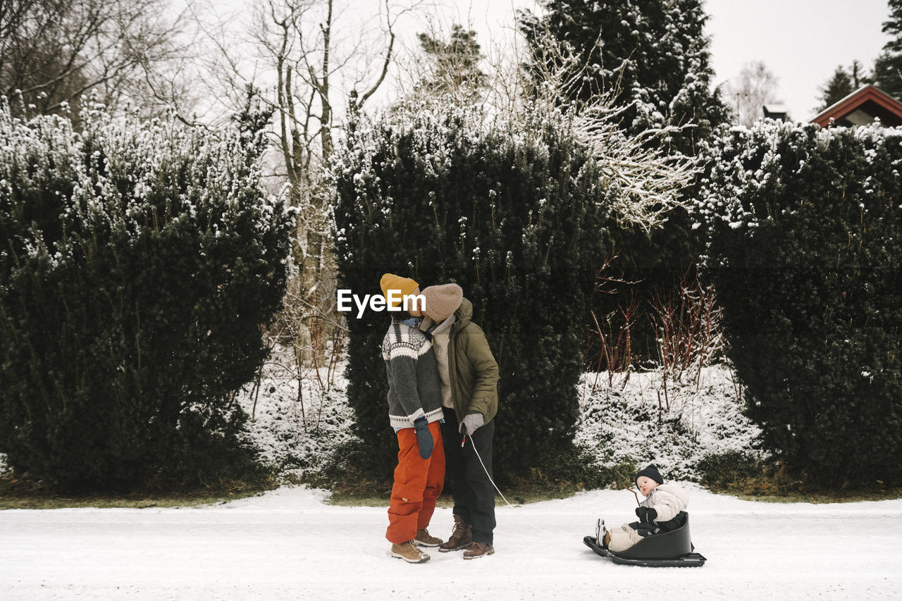 Gay couple kissing by daughter on toboggan during winter