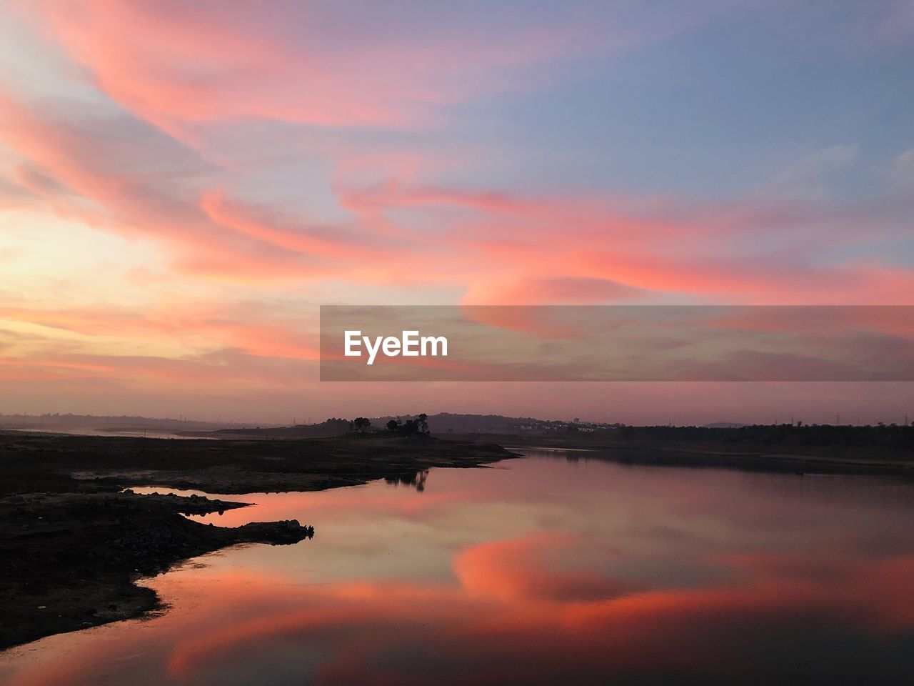 Scenic view of lake against dramatic sky during sunset