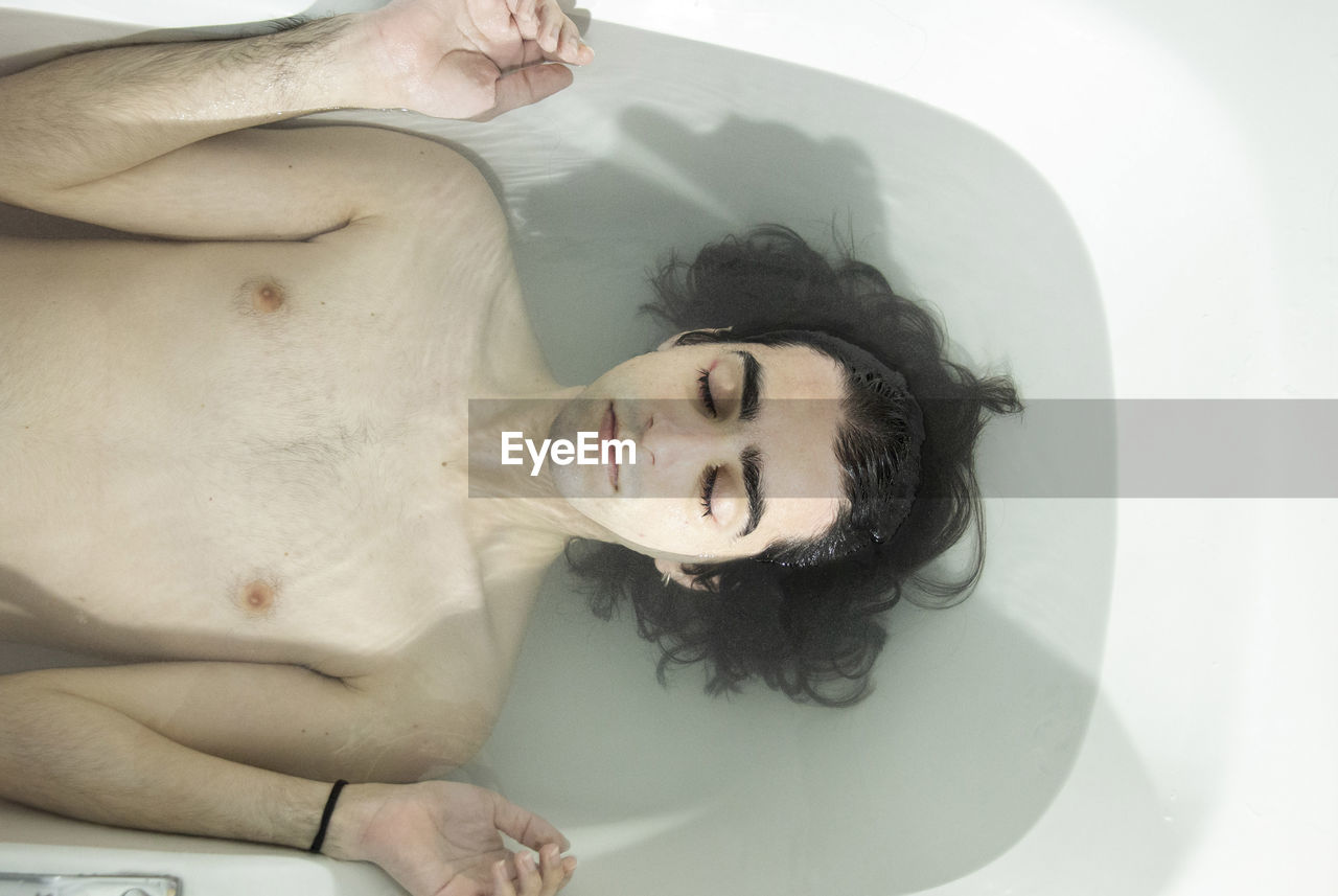 Shirtless man with eyes closed lying in bathtub