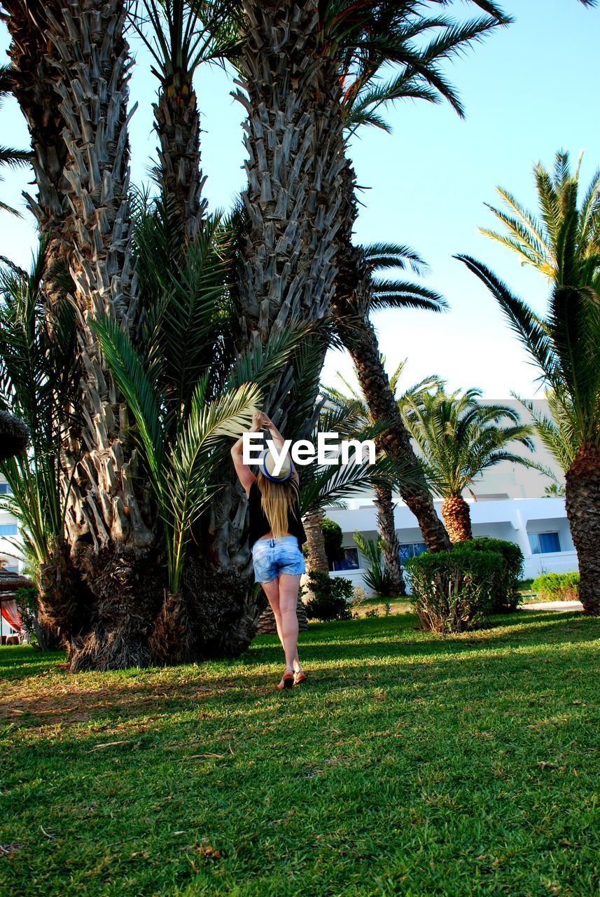 FULL LENGTH OF YOUNG WOMAN STANDING ON TREE TRUNK