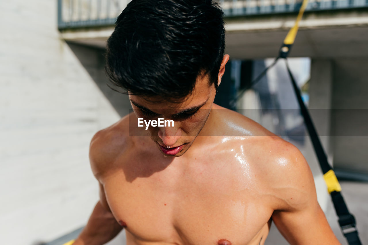 Determined male athlete with muscular body training on street with trx ropes and looking away