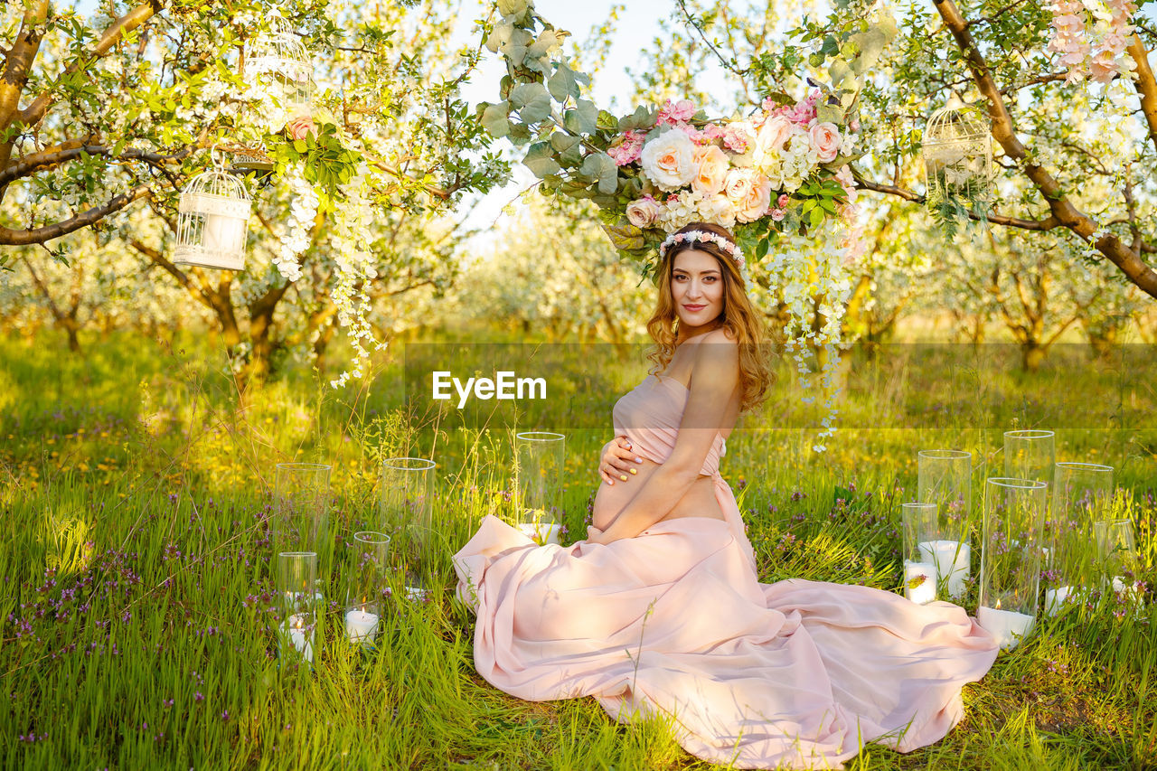 PORTRAIT OF BEAUTIFUL WOMAN WITH PINK FLOWERS AGAINST TREES