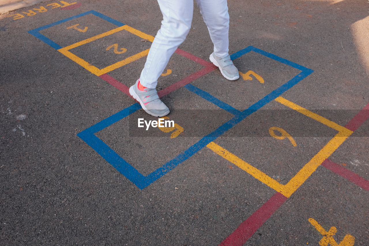 Low section of child playing hopscotch on road