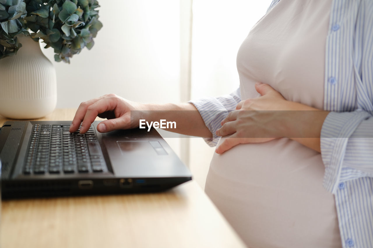 midsection of woman using laptop while sitting on table