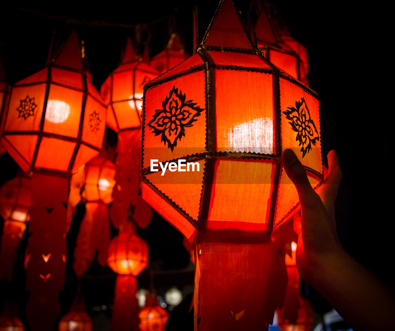 Close-up of person touching the red illuminated lantern in the street at night