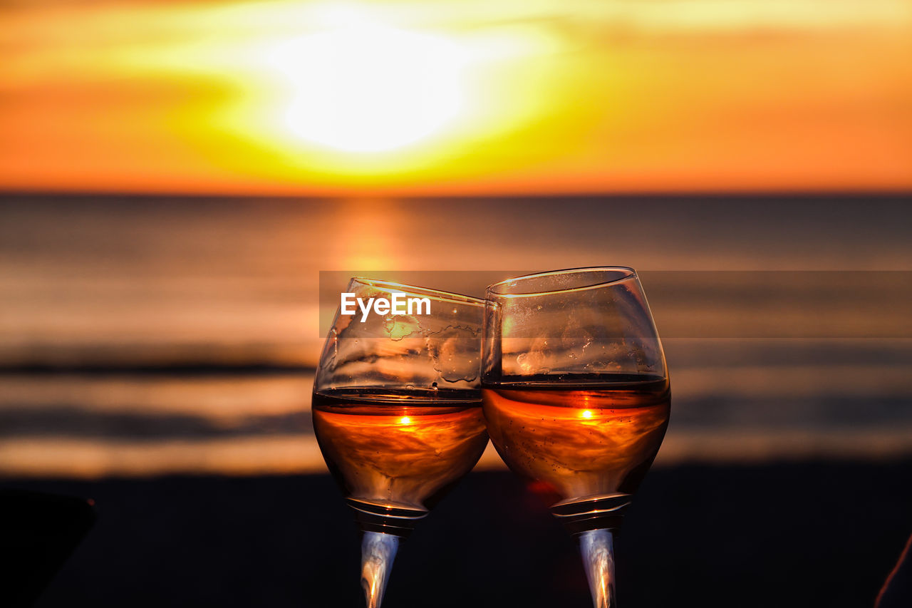 Close-up of beer glass on beach against sky during sunset