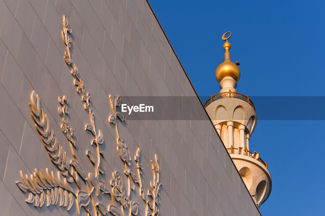 LOW ANGLE VIEW OF CROSS AMIDST BUILDINGS AGAINST CLEAR SKY