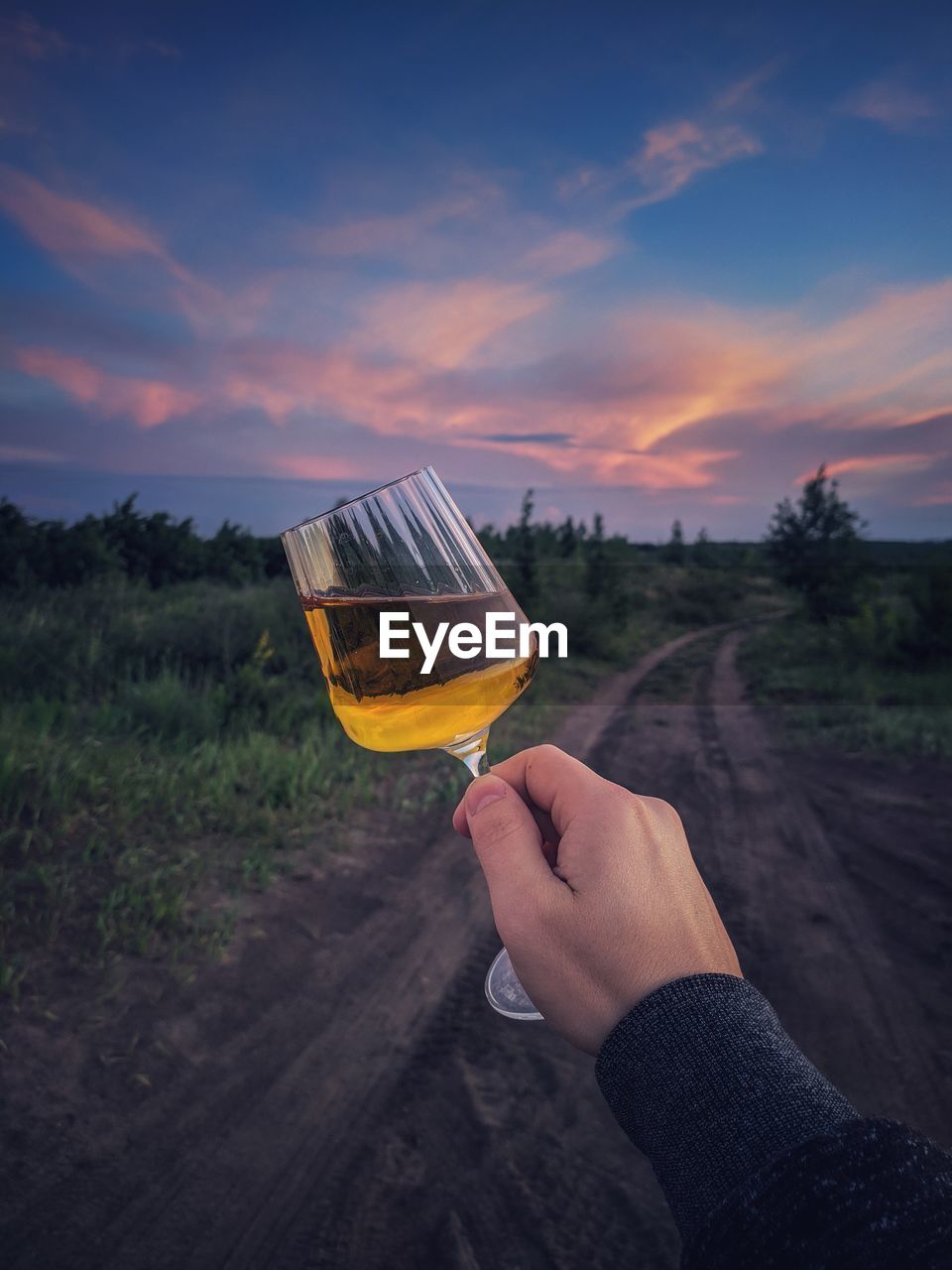 Midsection of person holding drink against sky during sunset