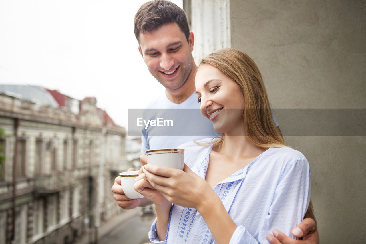 HAPPY YOUNG MAN HOLDING COFFEE CUP AGAINST WALL