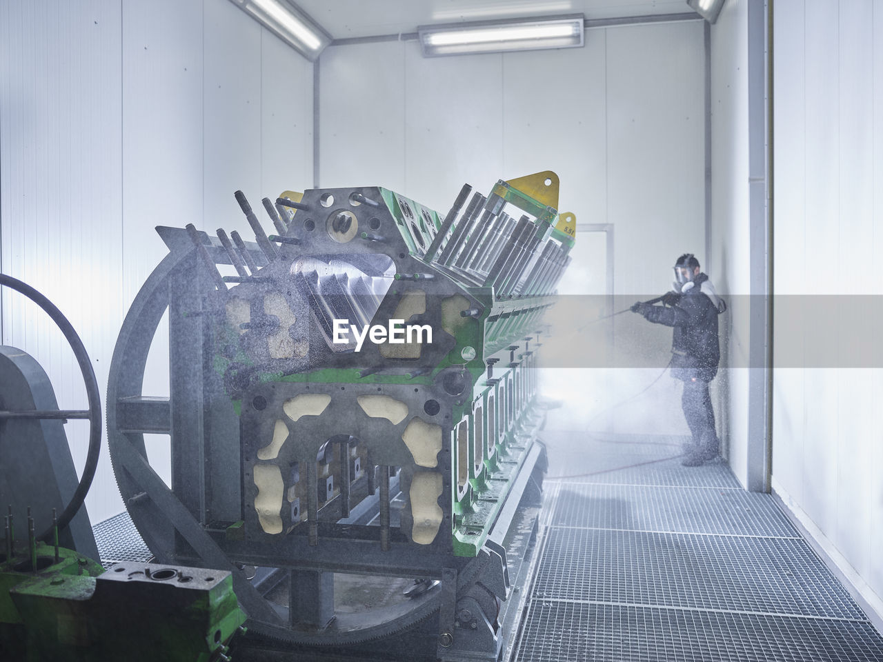 Worker cleaning engine block in washing bay