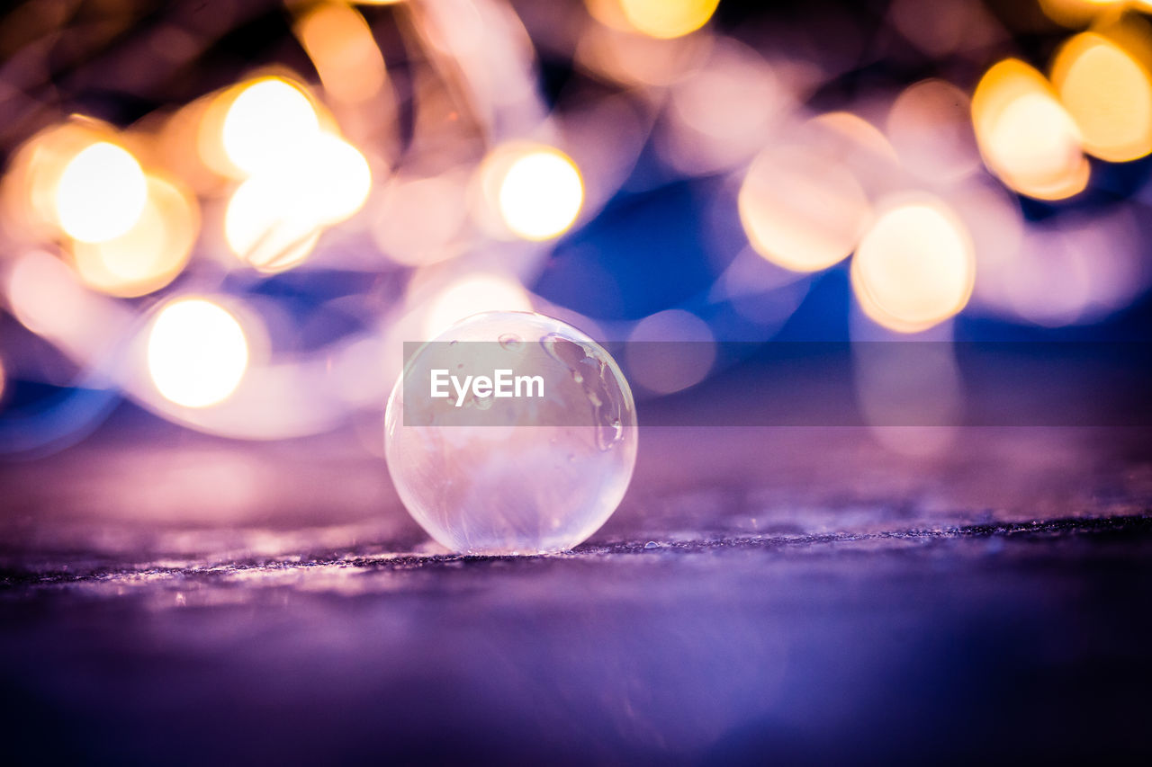 Close-up of crystal ball on field against illuminated christmas lights at night