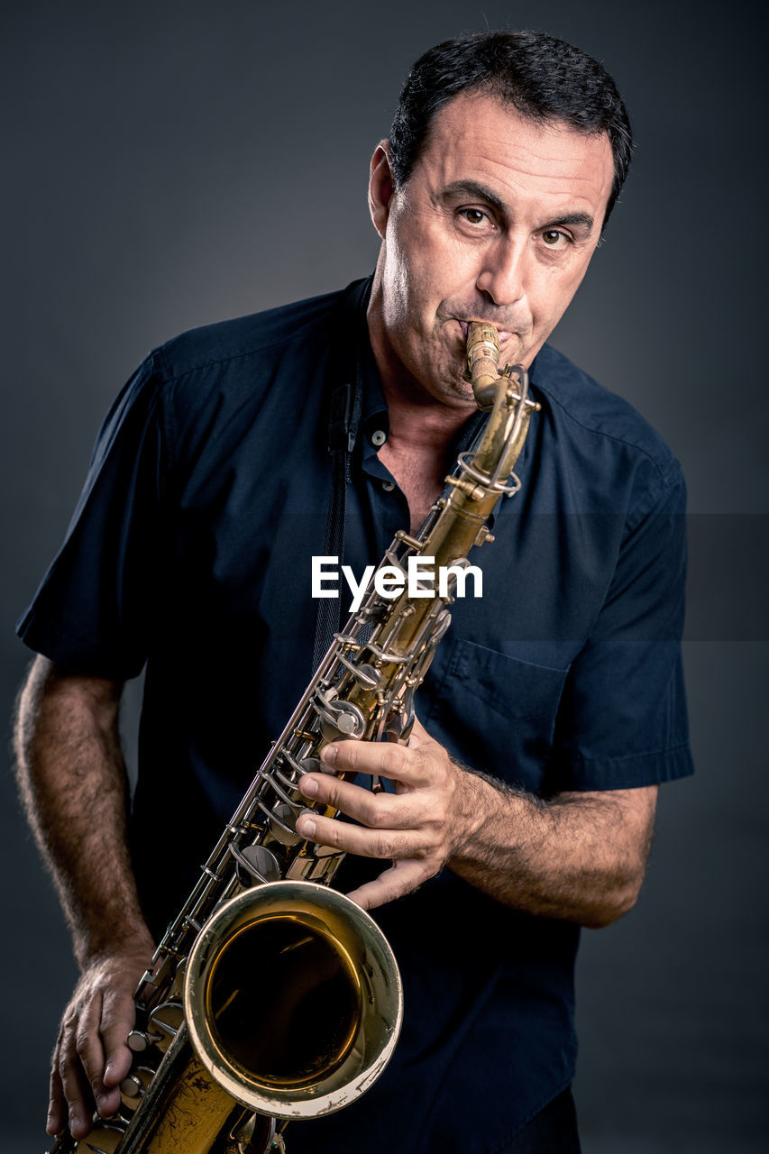 Portrait of mature man playing saxophone against black background