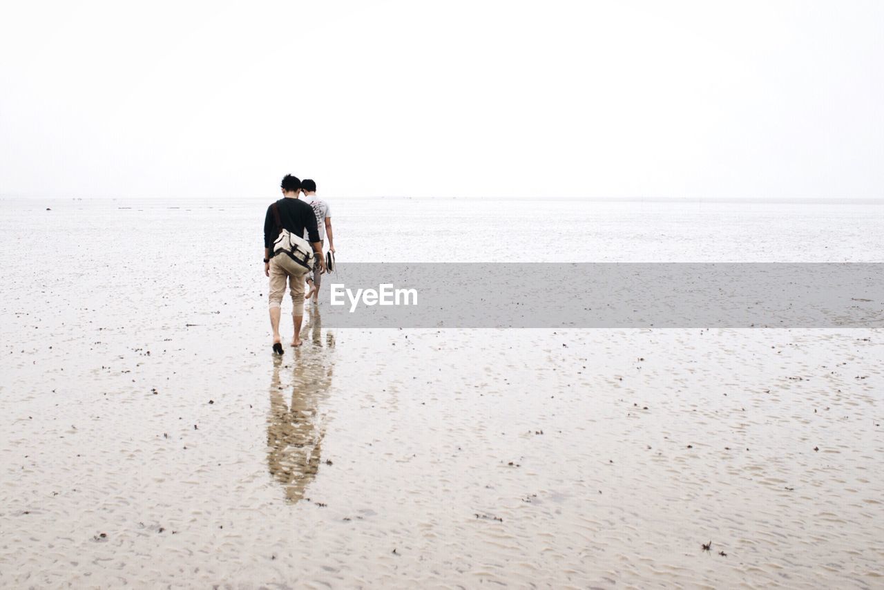 Rear view of men walking on beach