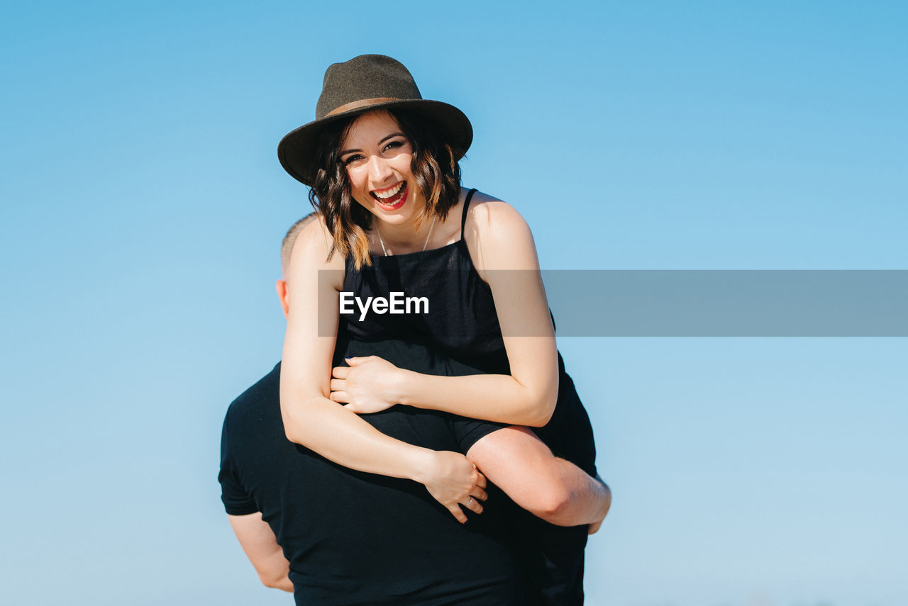 SMILING YOUNG WOMAN STANDING AGAINST SKY