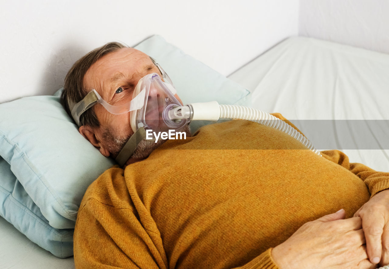 Senior man wearing oxygen mask lying on hospital bed