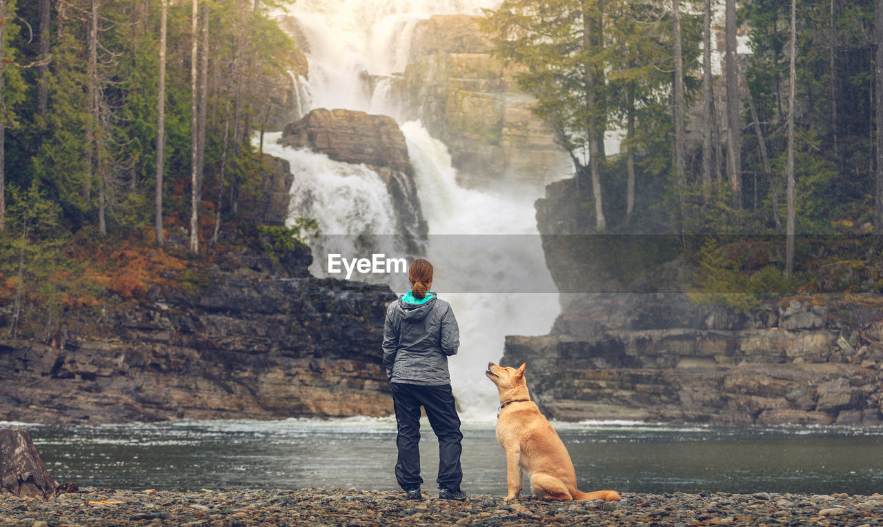 Full length of woman with dog by waterfall