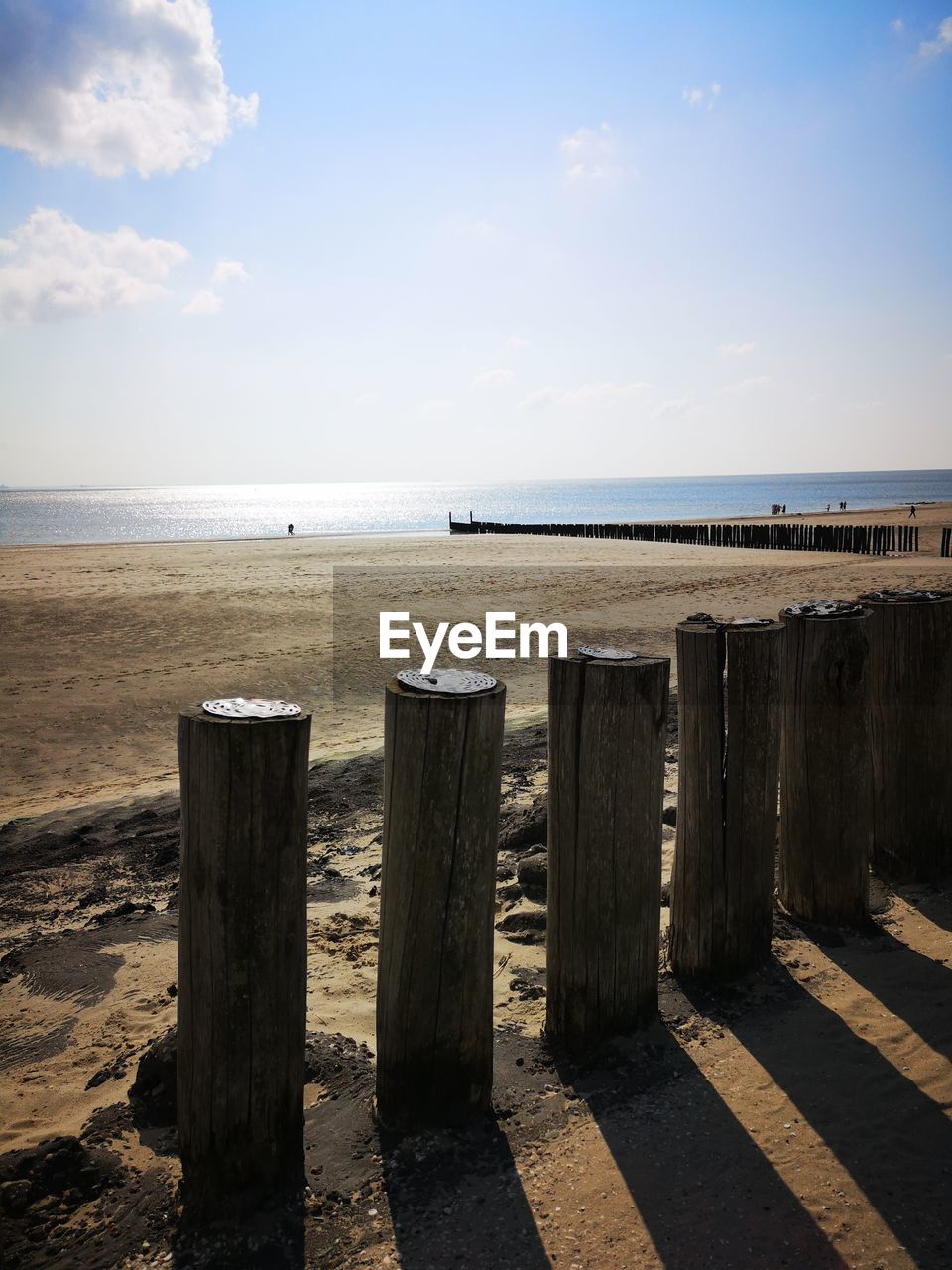 WOODEN POSTS ON SEA SHORE AGAINST SKY