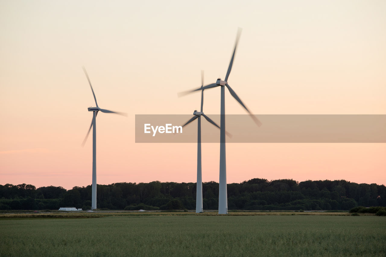 Windmills in motion on grassy field against clear sky during sunset