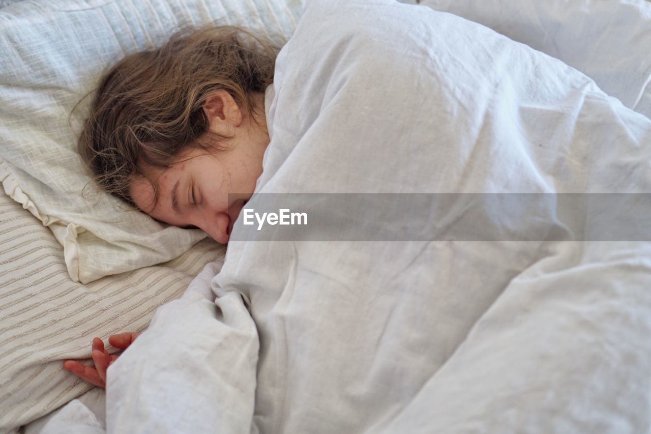 High angle view of smiling young woman sleeping on bed at home