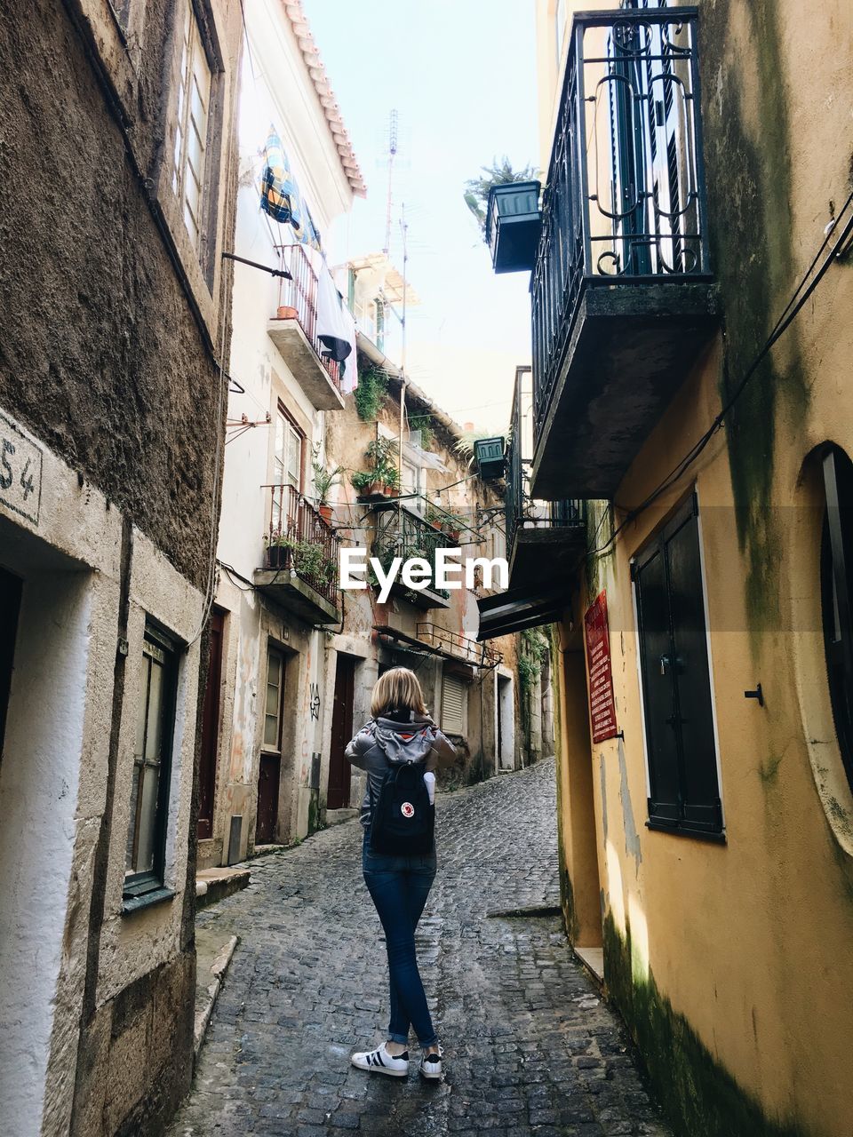 REAR VIEW OF WOMAN STANDING ON STREET AMIDST BUILDINGS