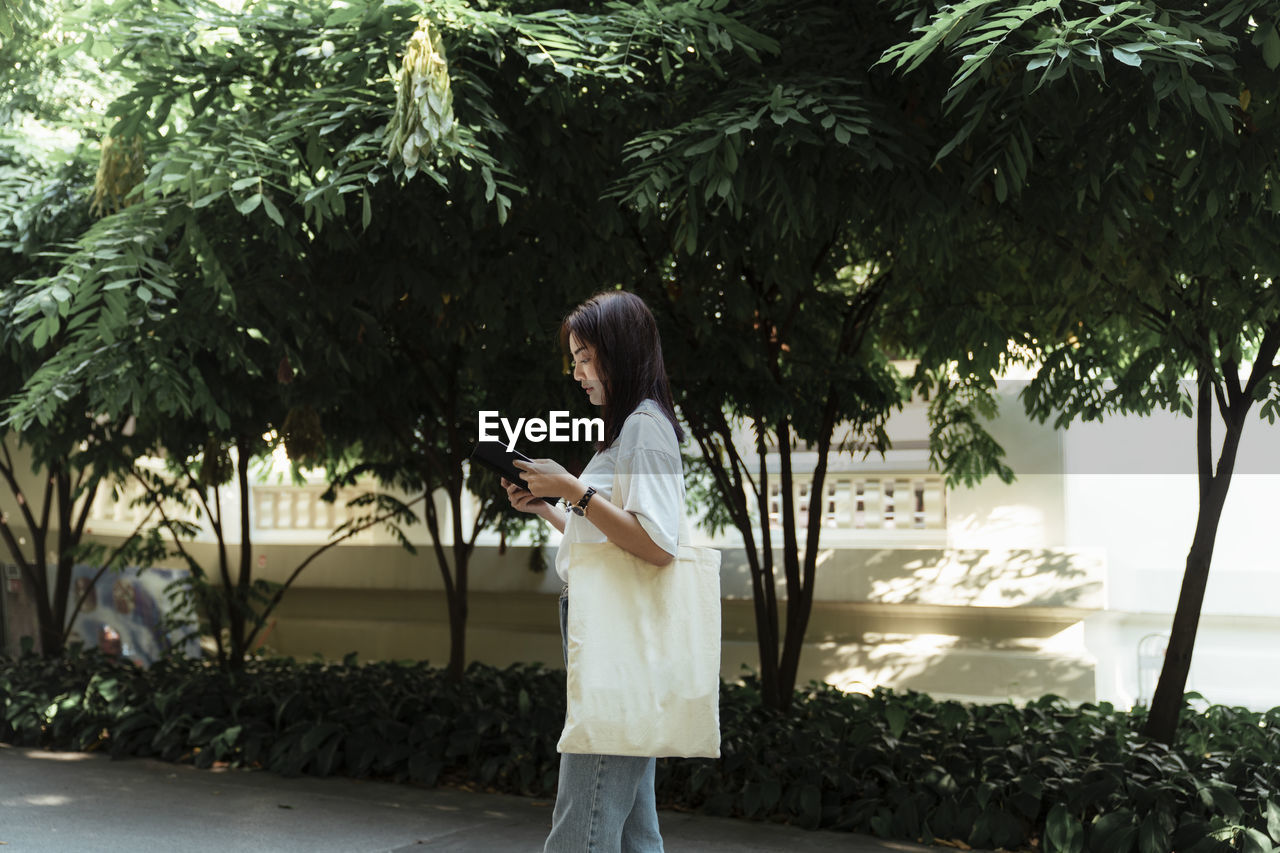 Side view of woman reading book while walking outdoors