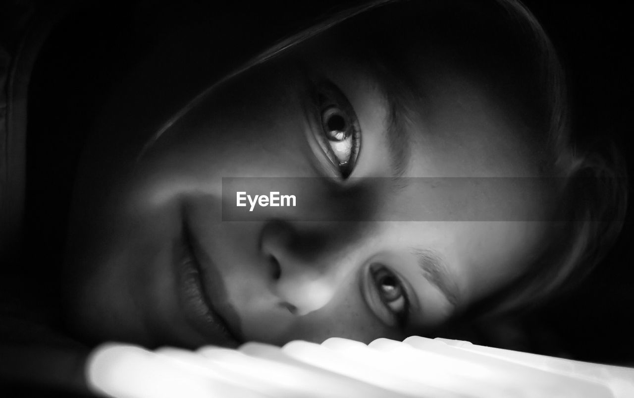 Close-up portrait of young woman lying by illuminated lighting equipment