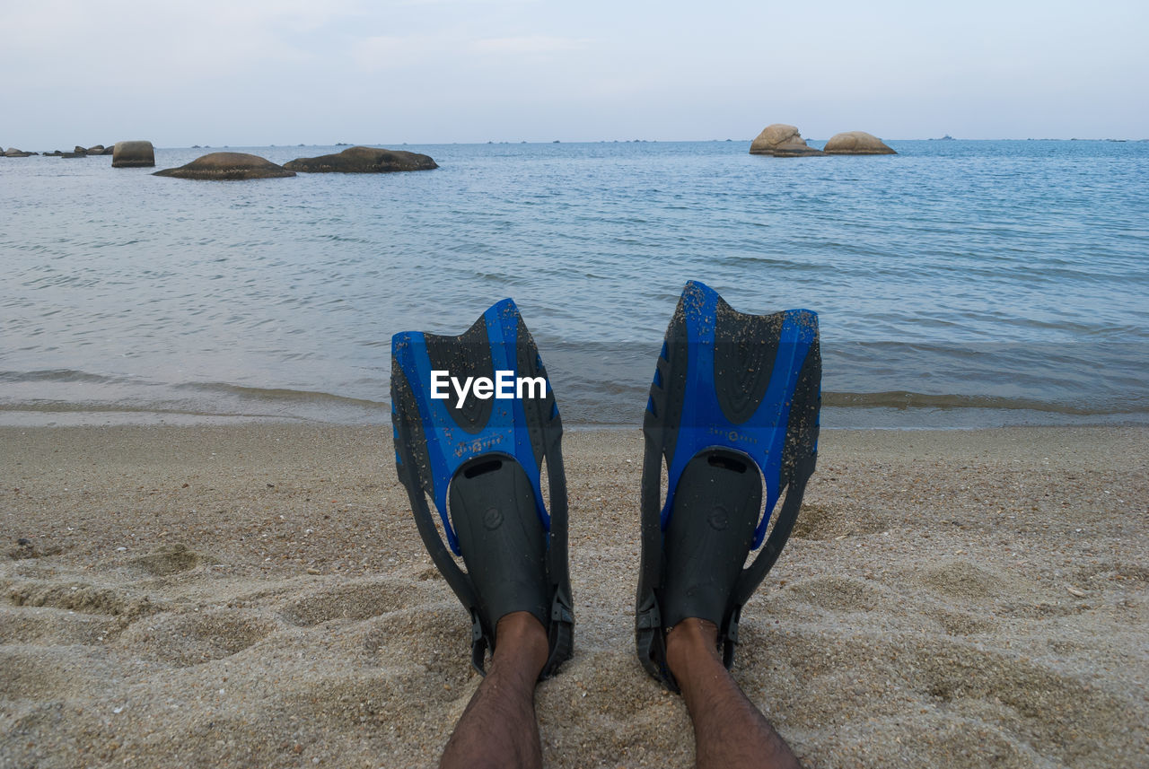 Low section of man wearing diving flippers at trikora beach against sky