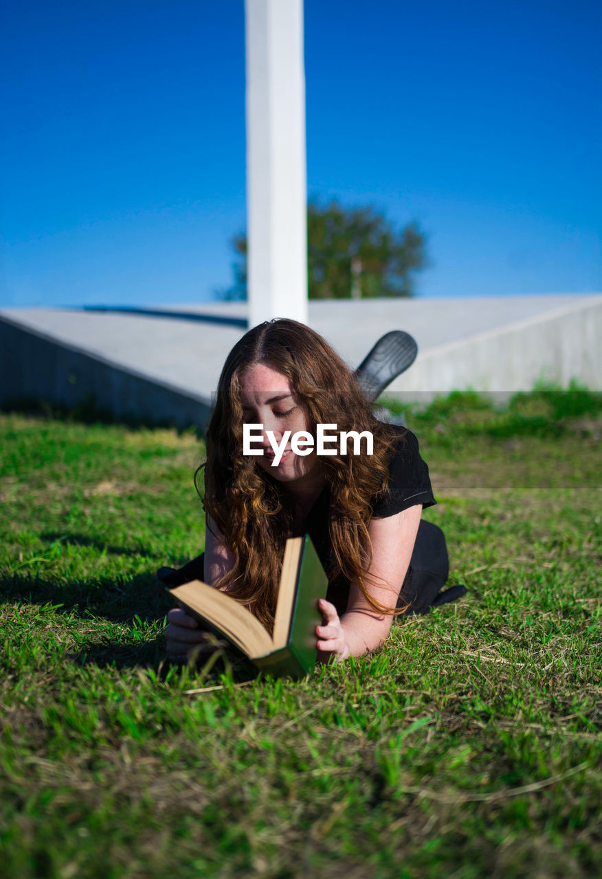 Woman reading book on field against sky