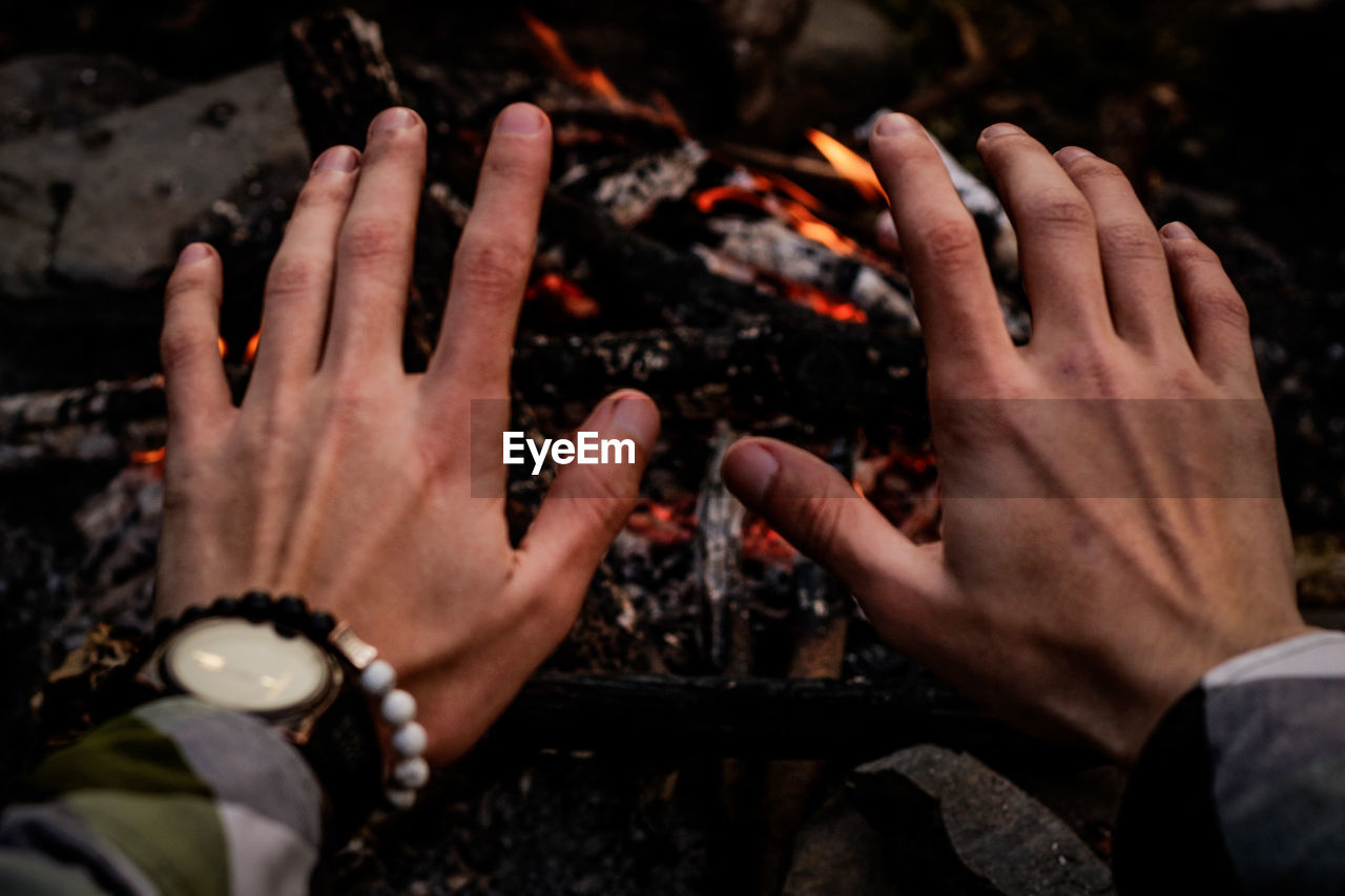 Cropped hands of man gesturing against campfire