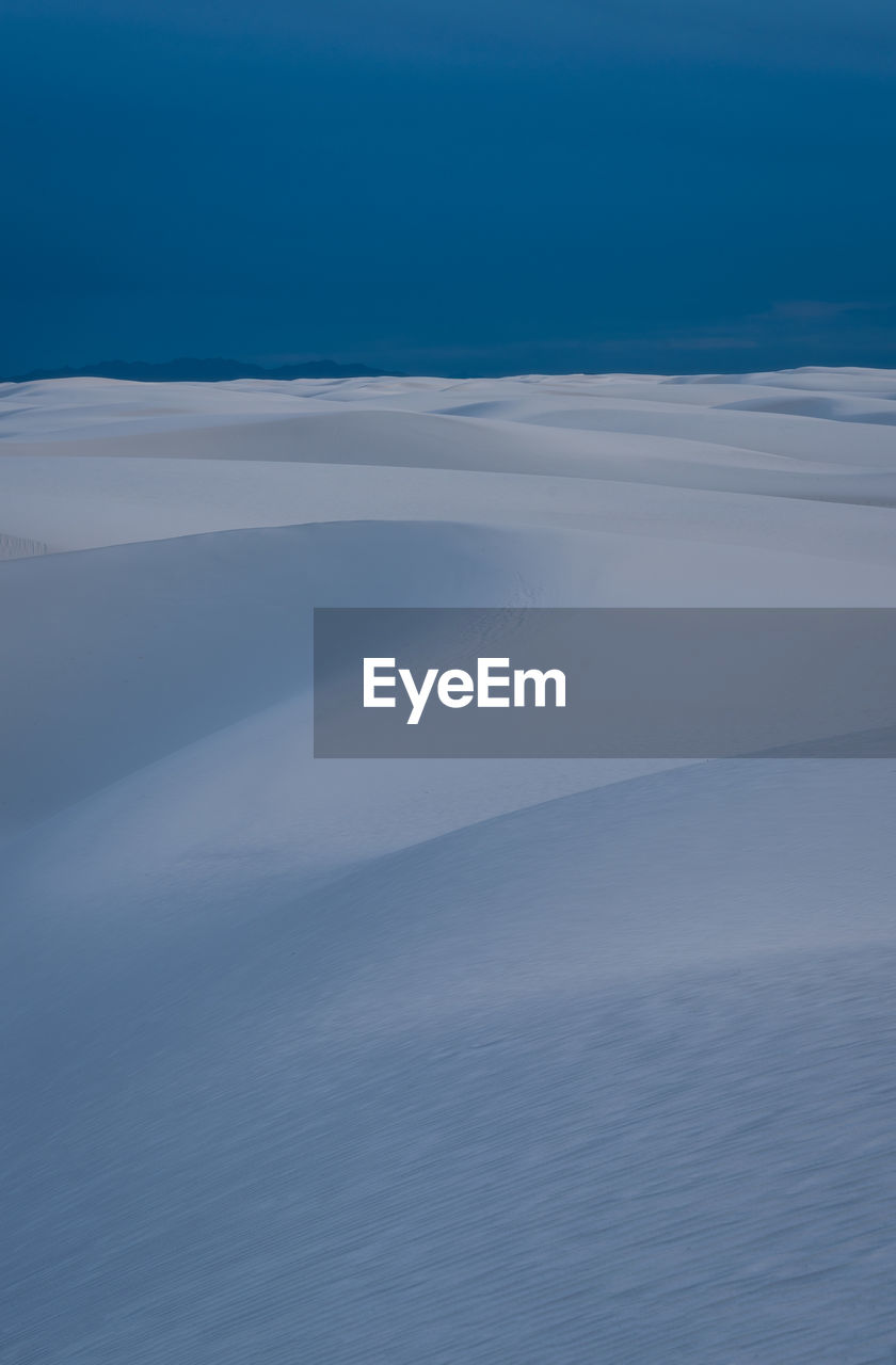 Scenic view of sand covered landscape against blue sky in white sands national park